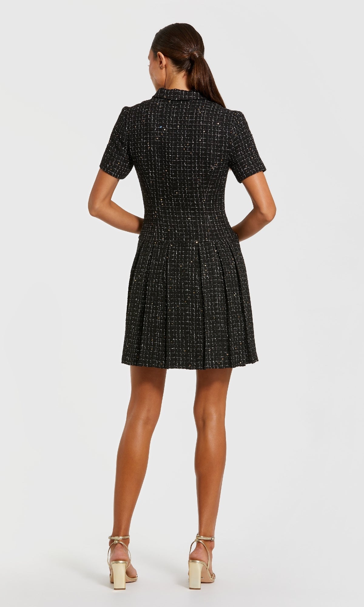 A woman stands facing away in the Mac Duggal 81200 Tweed-Blazer Short Party Dress with a pleated skirt and beige heels, perfect for semi-formal events, set against a plain white background.